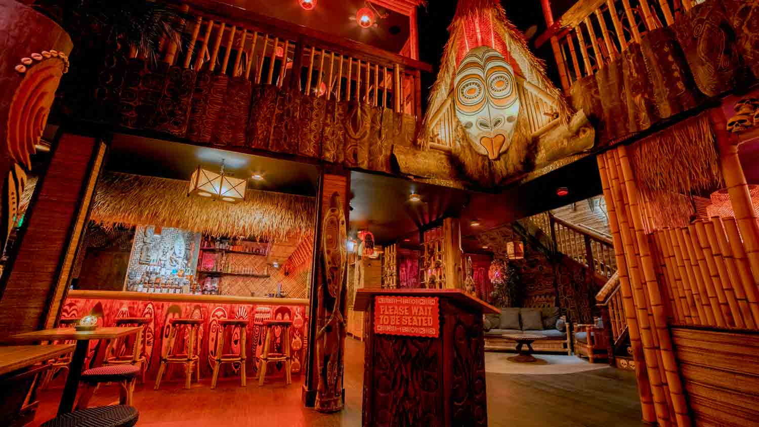 The Inferno Room’s bamboo-lined interior, with carved bar stools, a large hanging mask, and a host stand beneath the balcony.